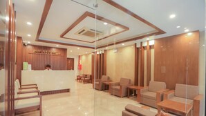 A hotel reception area with a wooden reception desk, several seating areas with chairs and sofas, and a polished floor.