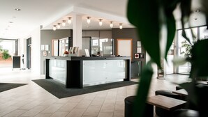 A modern hotel lobby with a reception desk, seating area, and large windows. - Hotel Ochsen (Merklingen)