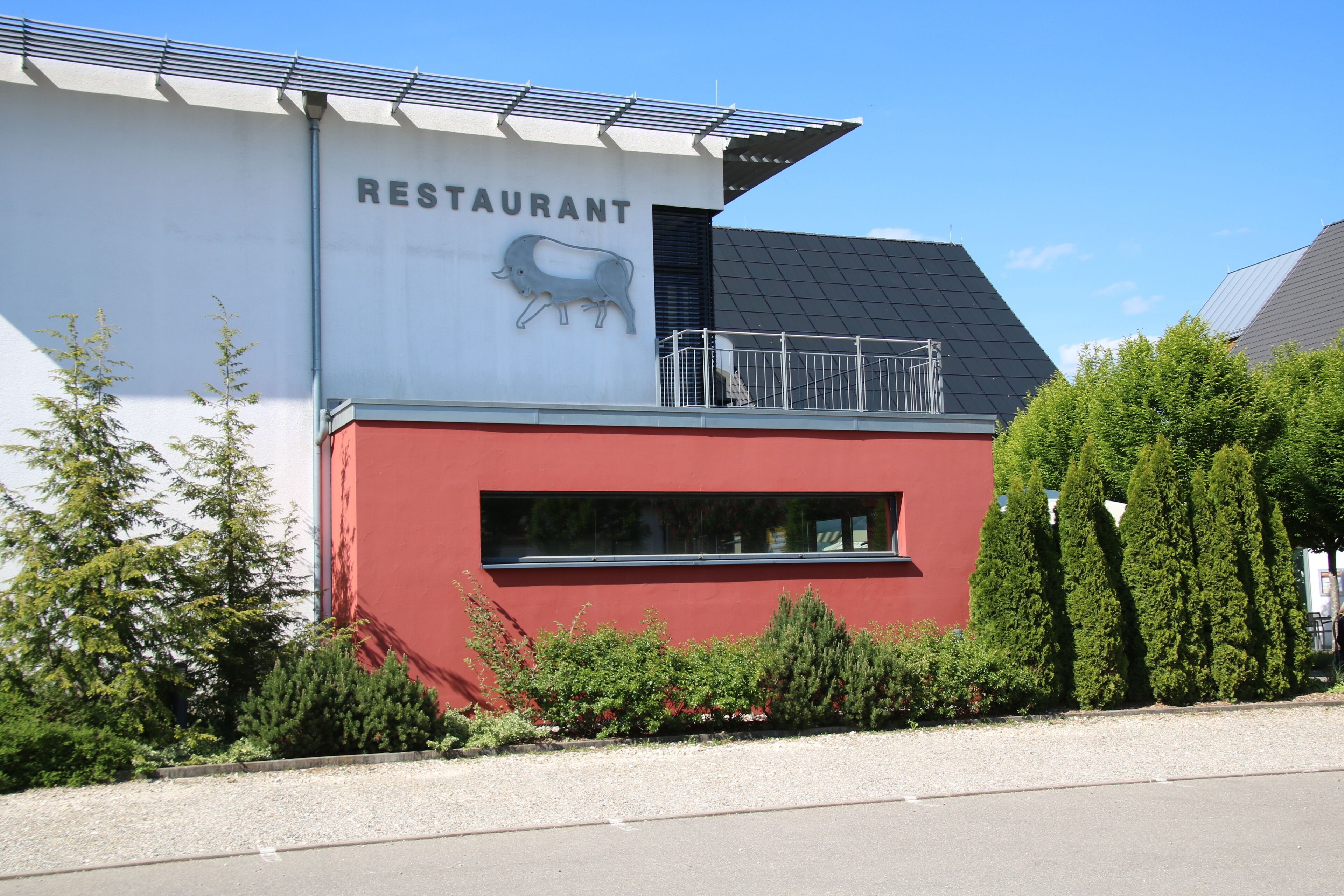 A restaurant with a red and white exterior, solar panels on the roof, and a pig logo.