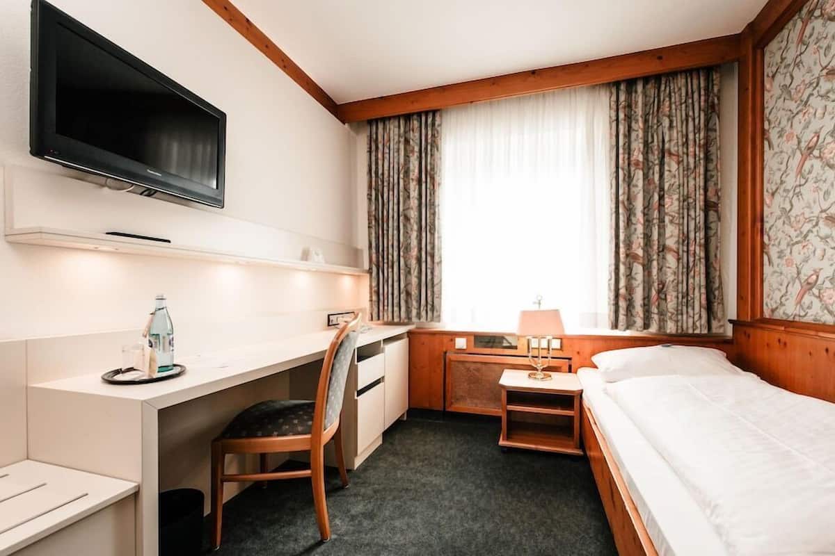 A hotel room with a bed, desk, chair, television, and curtains.