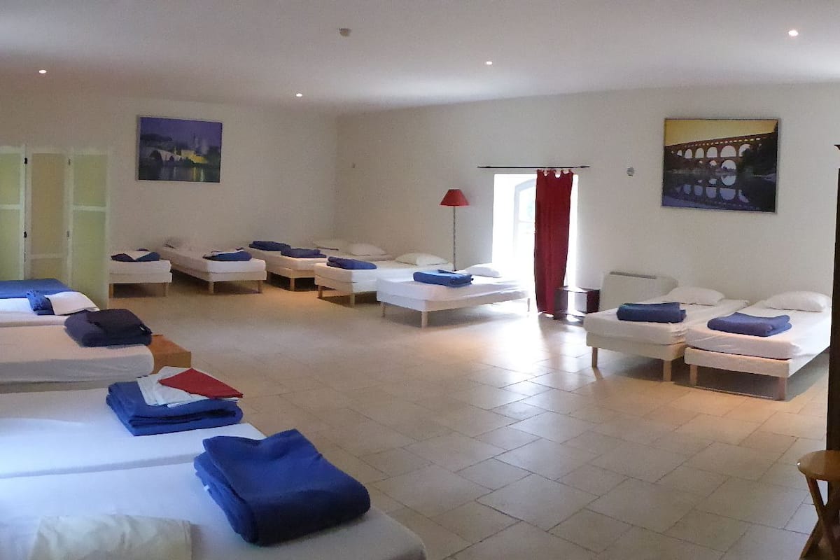Ein Zimmer mit mehreren nebeneinanderstehenden Betten, einer roten Lampe und einem Bild an der Wand.
