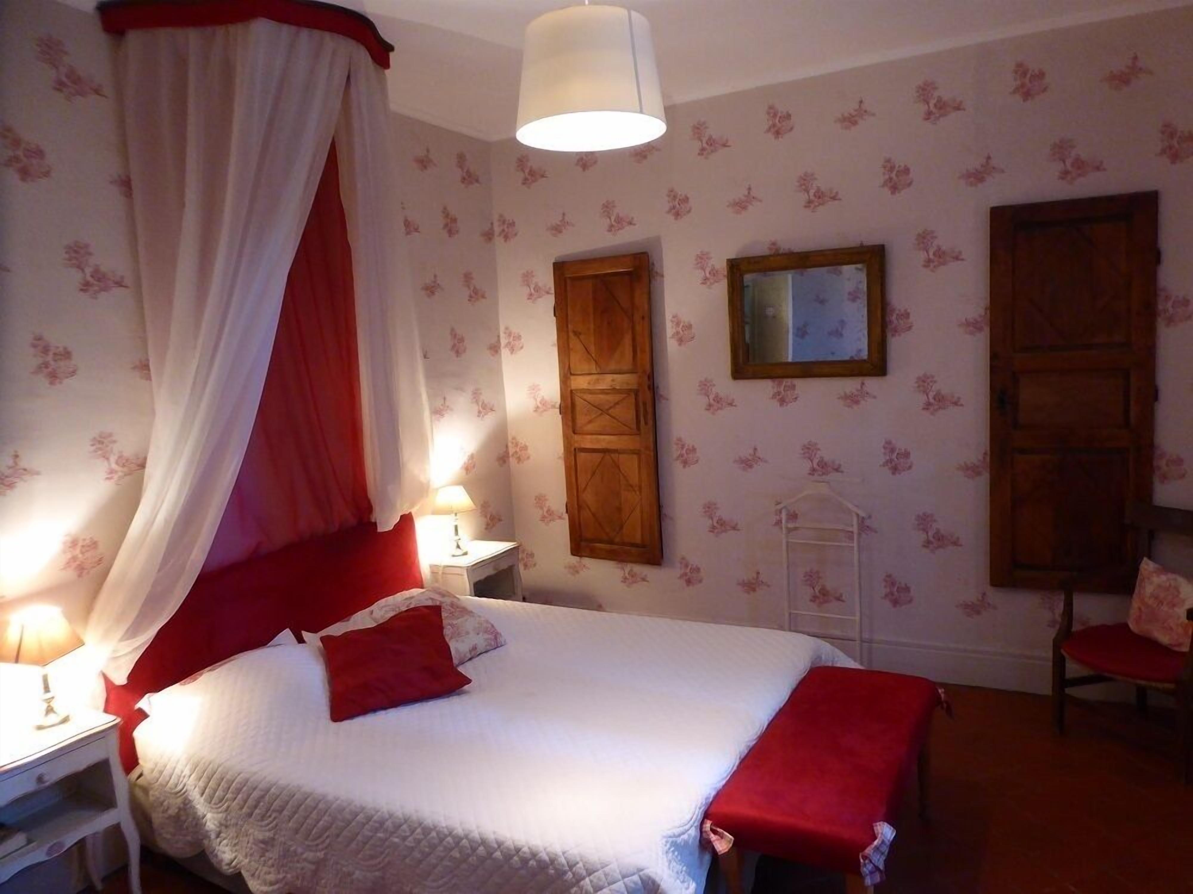 Un dormitorio con cama con dosel, un armario de madera, una mesita de noche con lámpara y una silla.