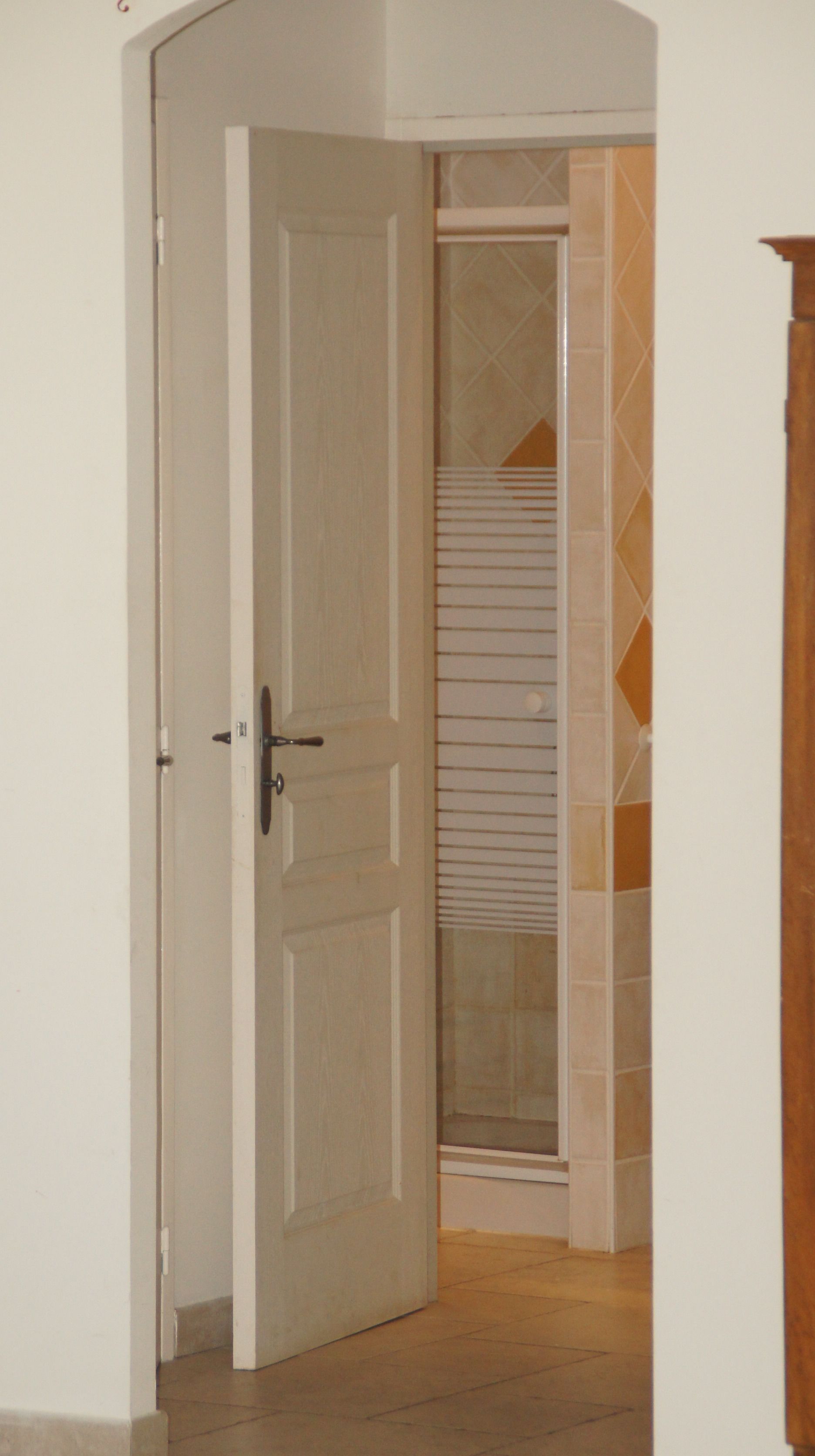 Un couloir avec une porte fermée, un mur recouvert de carreaux et un plancher en bois.
