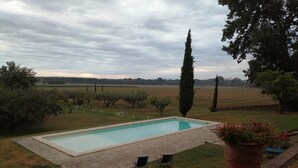 A rectangular swimming pool with a paved deck, surrounded by a grassy area with trees and shrubs. There are two chairs and a large potted plant near the pool. - Domaine de Lamartine chambres d'hotes (Pont-Saint-Esprit)