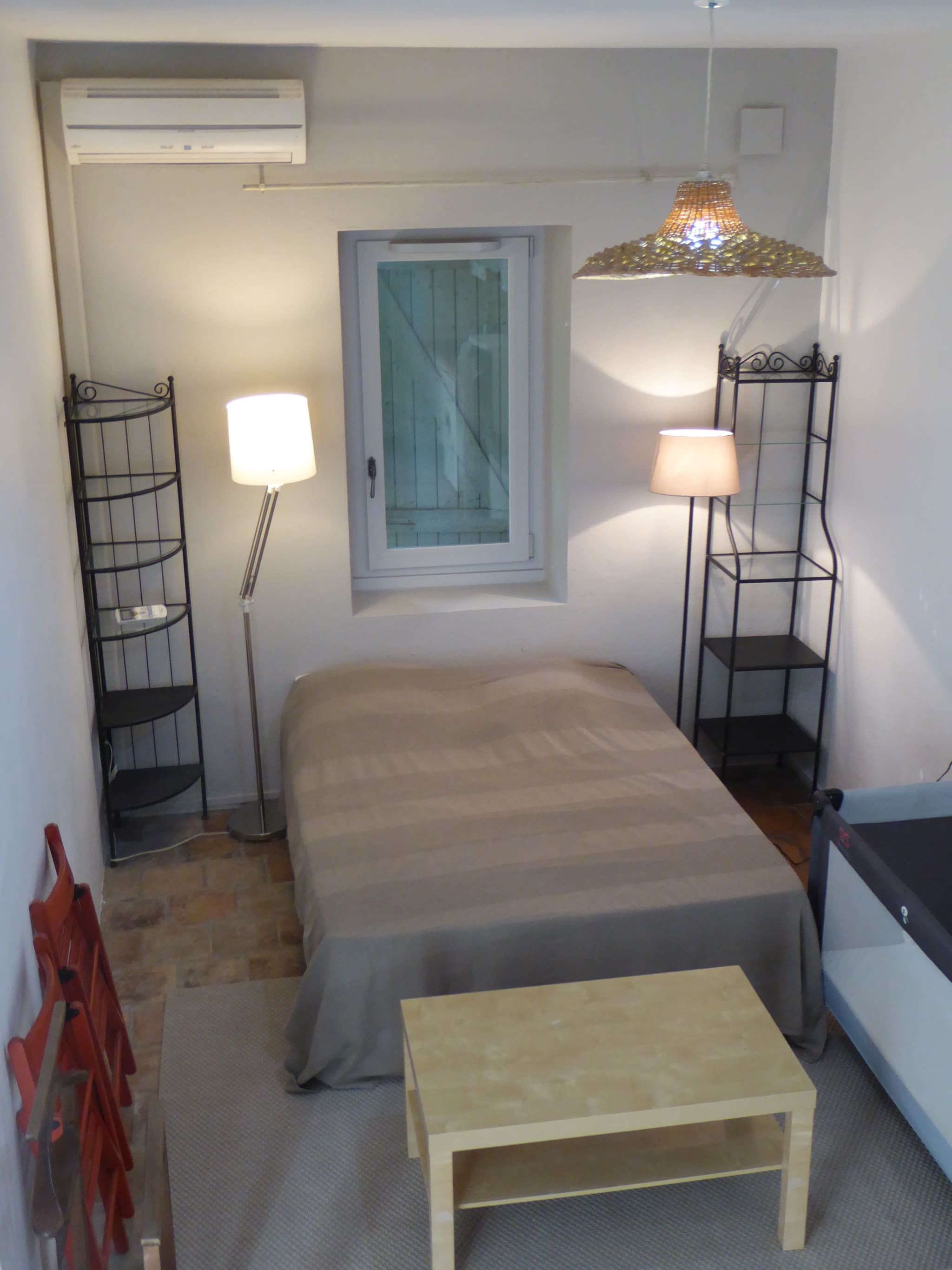 Un dormitorio pequeño con cama, mesita de noche, lámpara, estante y aire acondicionado.