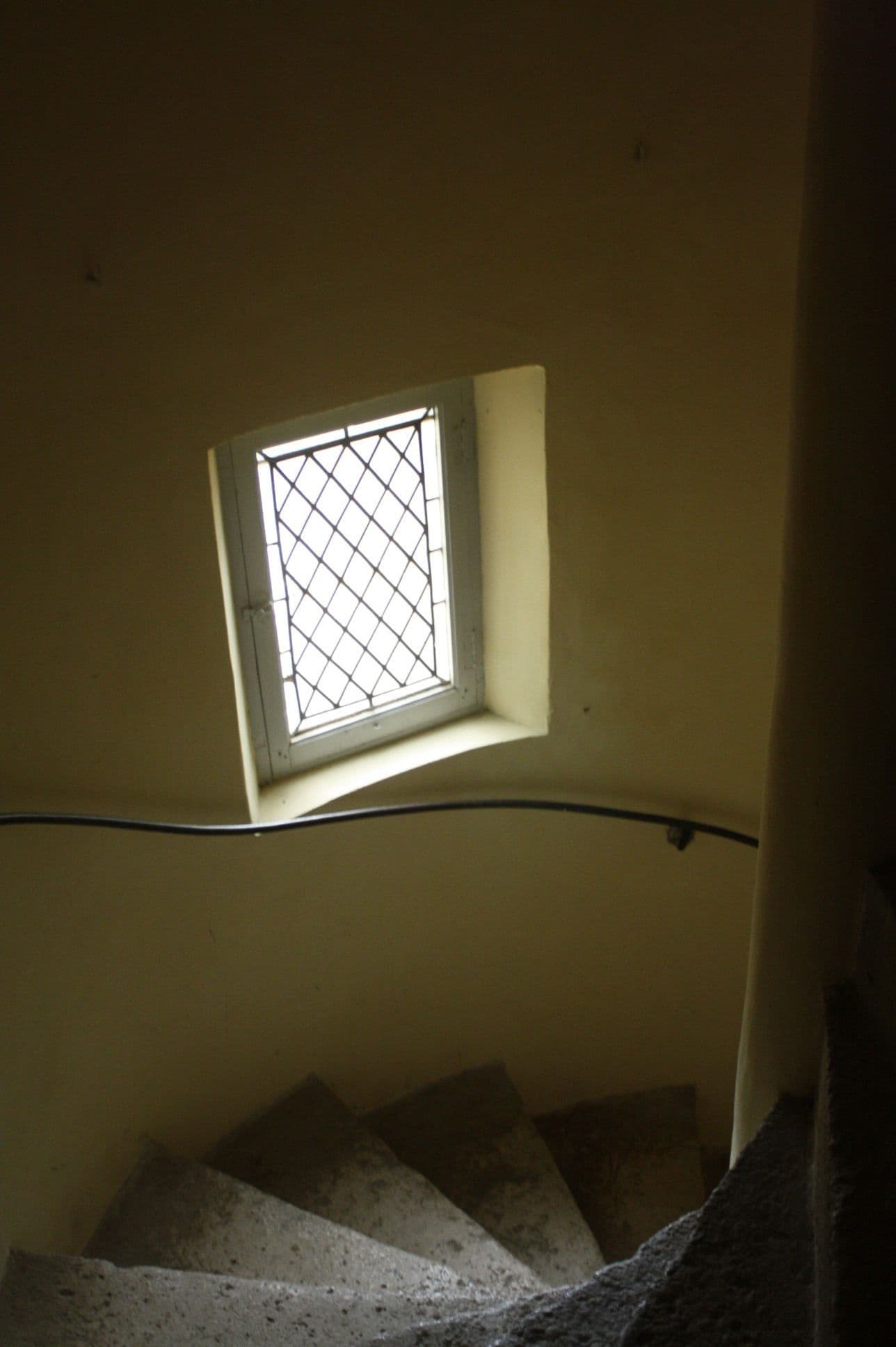A small window with a metal grid, a concrete staircase, and a white wall.