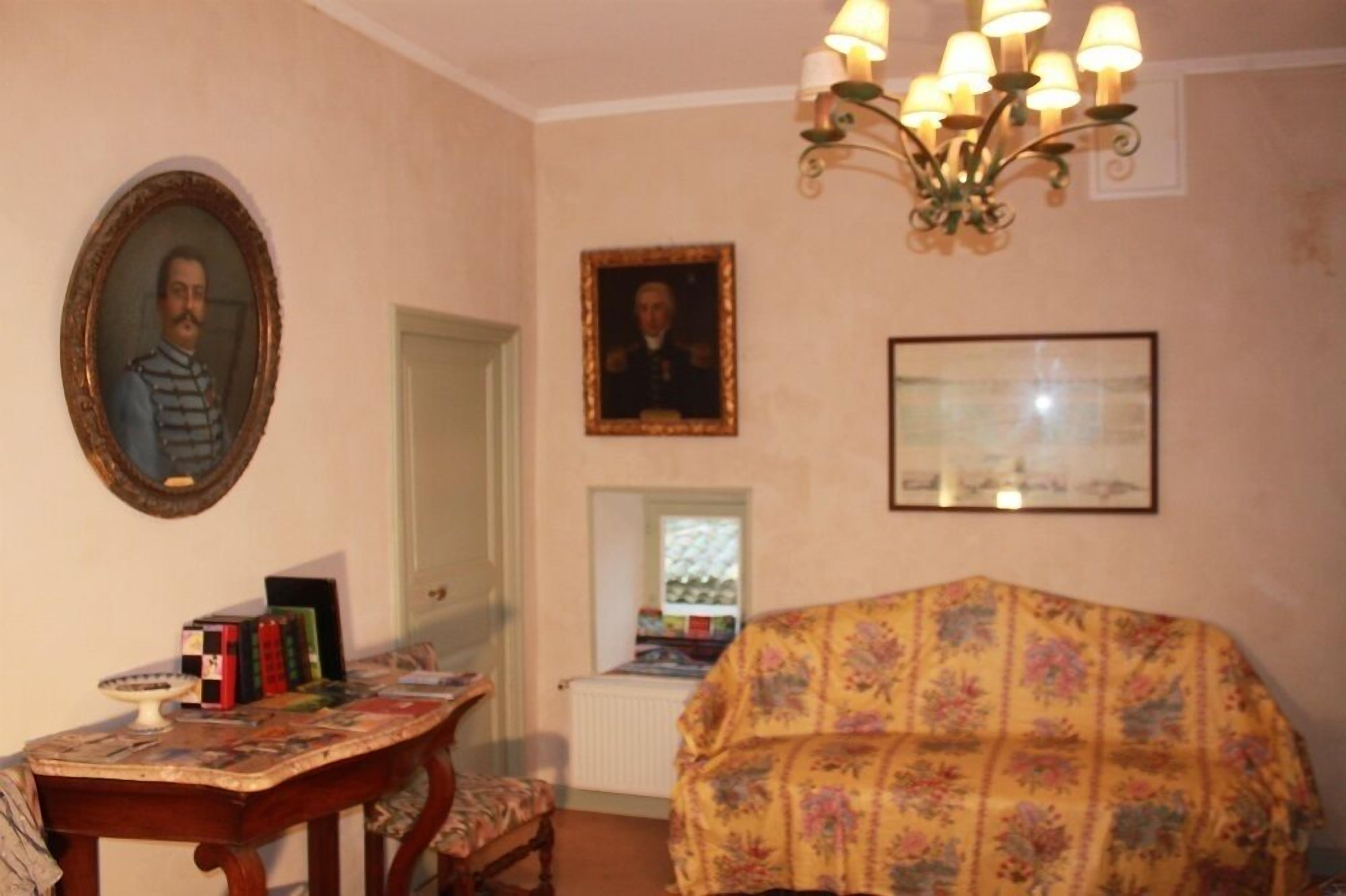 A room with a wooden table, a floral-covered sofa, a chandelier, and framed pictures on the walls.
