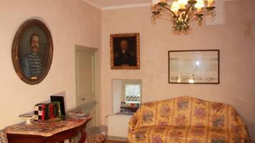 A room with a wooden table, a floral-covered sofa, a chandelier, and framed pictures on the walls.