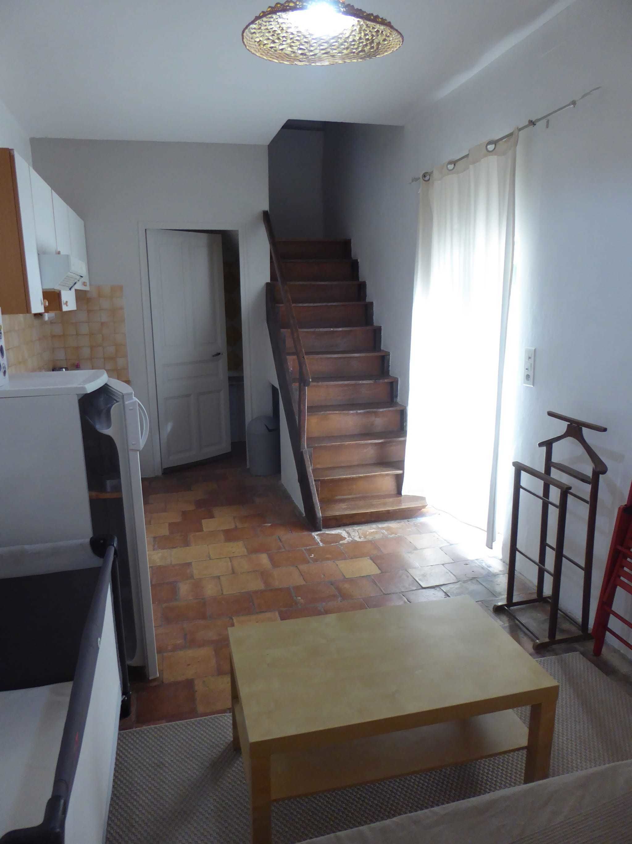 A kitchen with a wooden staircase leading to a door, a dining table, and a hanging light fixture.