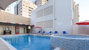 A swimming pool with blue and white mosaic tiles, surrounded by lounge chairs and umbrellas.