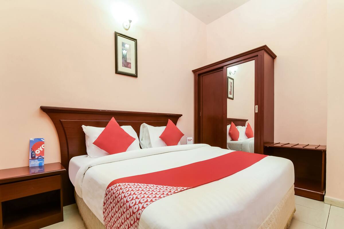 A hotel room with a large bed, a nightstand, a wardrobe, and a framed picture on the wall.