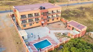 A multi-story building with a swimming pool, surrounded by a paved area and a road. - Leosim Hotel (Pakwach)