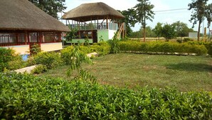 A well-maintained garden with a lawn, a thatched-roof structure, and a building with a green facade. - Leosim Hotel (Pakwach)