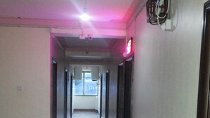 A corridor with a ceiling fan, a security camera, and a red exit sign. - Leosim Hotel (Pakwach)