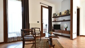 A living room with a wooden table, two chairs, a TV, and a bookshelf. - Il Terrazzo B&B (Romagnano Sesia)