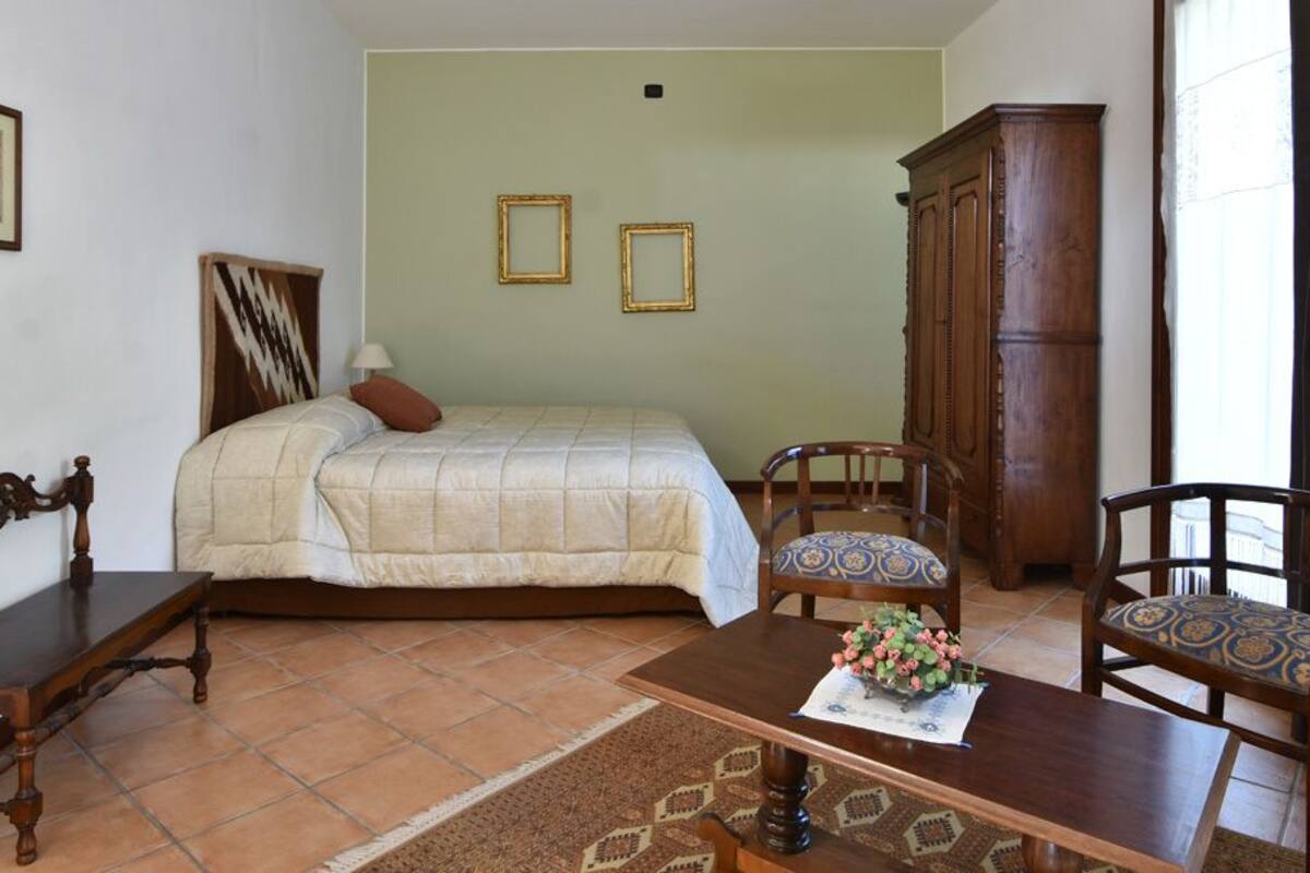 Une chambre à coucher comprenant un lit, deux chaises, un banc en bois, une table avec un vase de fleurs, une carte accrochée au mur et un radiateur.