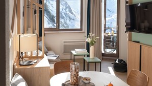 A modern hotel room with a dining area, a TV, a window with a mountain view, and a staircase. - Résidence Pierre & Vacances Capella (Morzine)