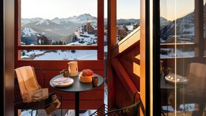 A balcony with a table set for two, a chair, and a view of snow-covered mountains. - Résidence Pierre & Vacances Capella (Morzine)
