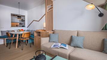 A modern living room with a sofa, a dining table with chairs, a kettle, and a book on the sofa.