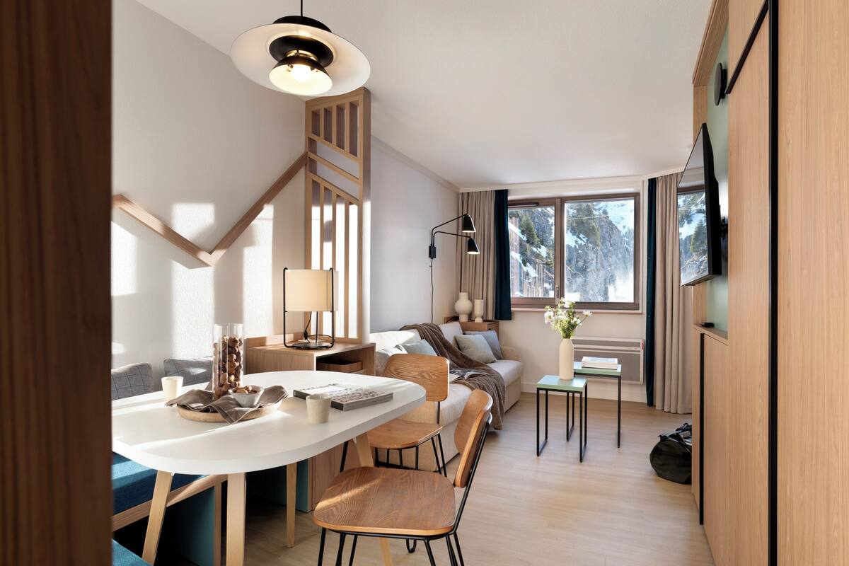 A modern interior with a dining area, sofa, TV, and a view of snowy mountains.