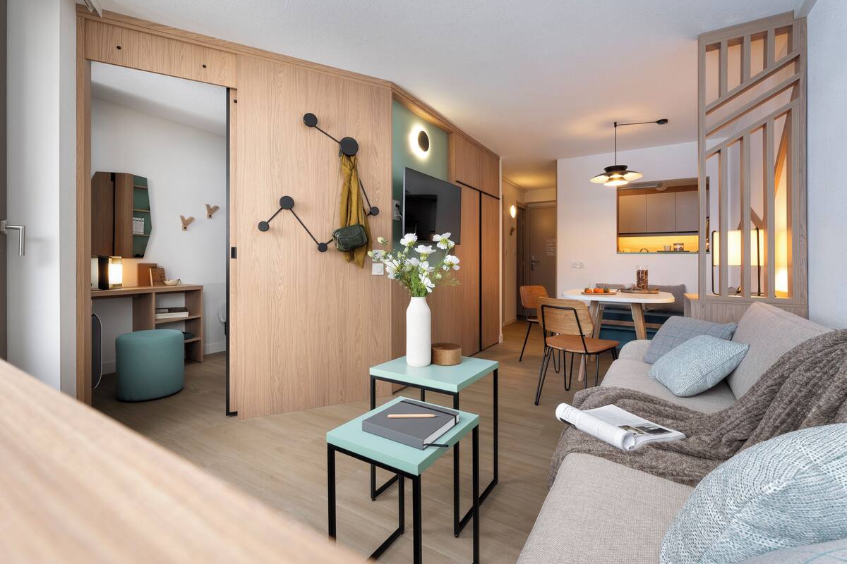 A modern living room with a sofa, a small table, a TV, and a dining area.