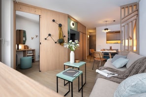A modern living room with a sofa, a small table, a TV, and a dining area. - Résidence Pierre & Vacances Capella (Morzine)
