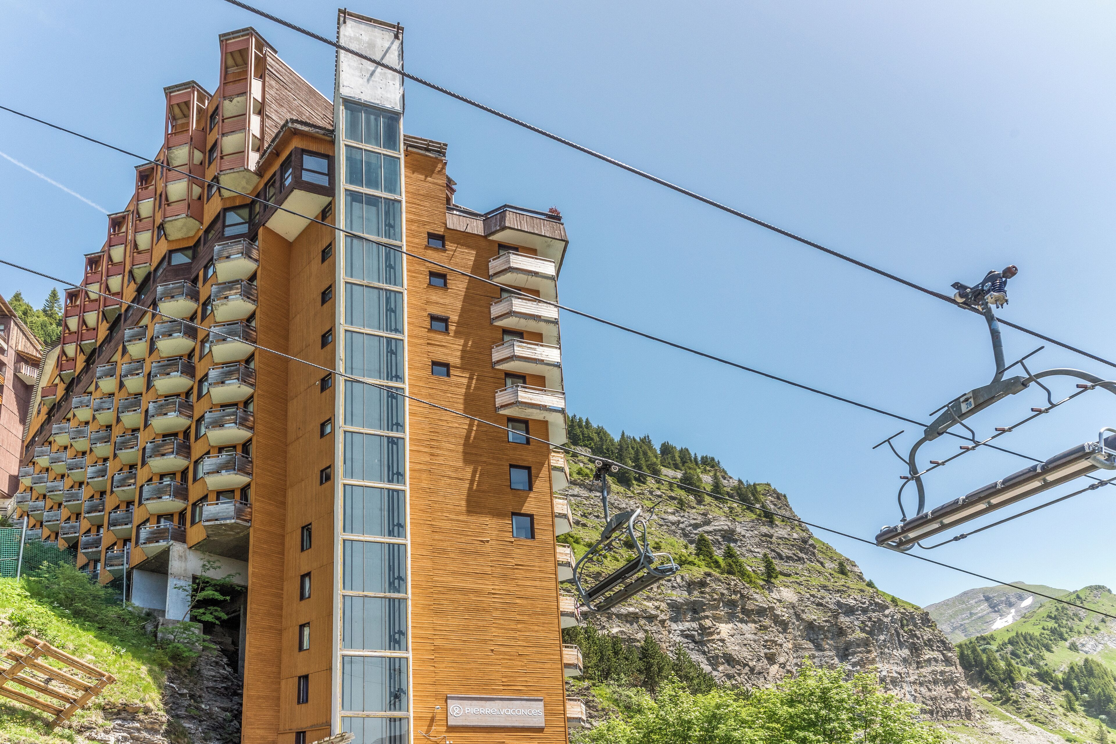A multi-story building with balconies, a ski lift, and a mountainous backdrop.