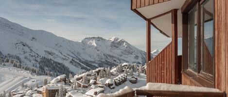 A wooden chalet with a balcony overlooking a snow-covered mountain village.