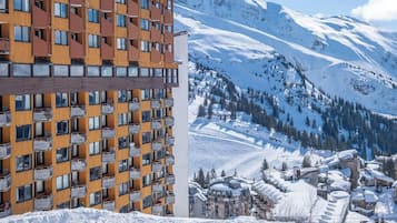 A modern hotel with multiple balconies, set against a snowy mountain backdrop.