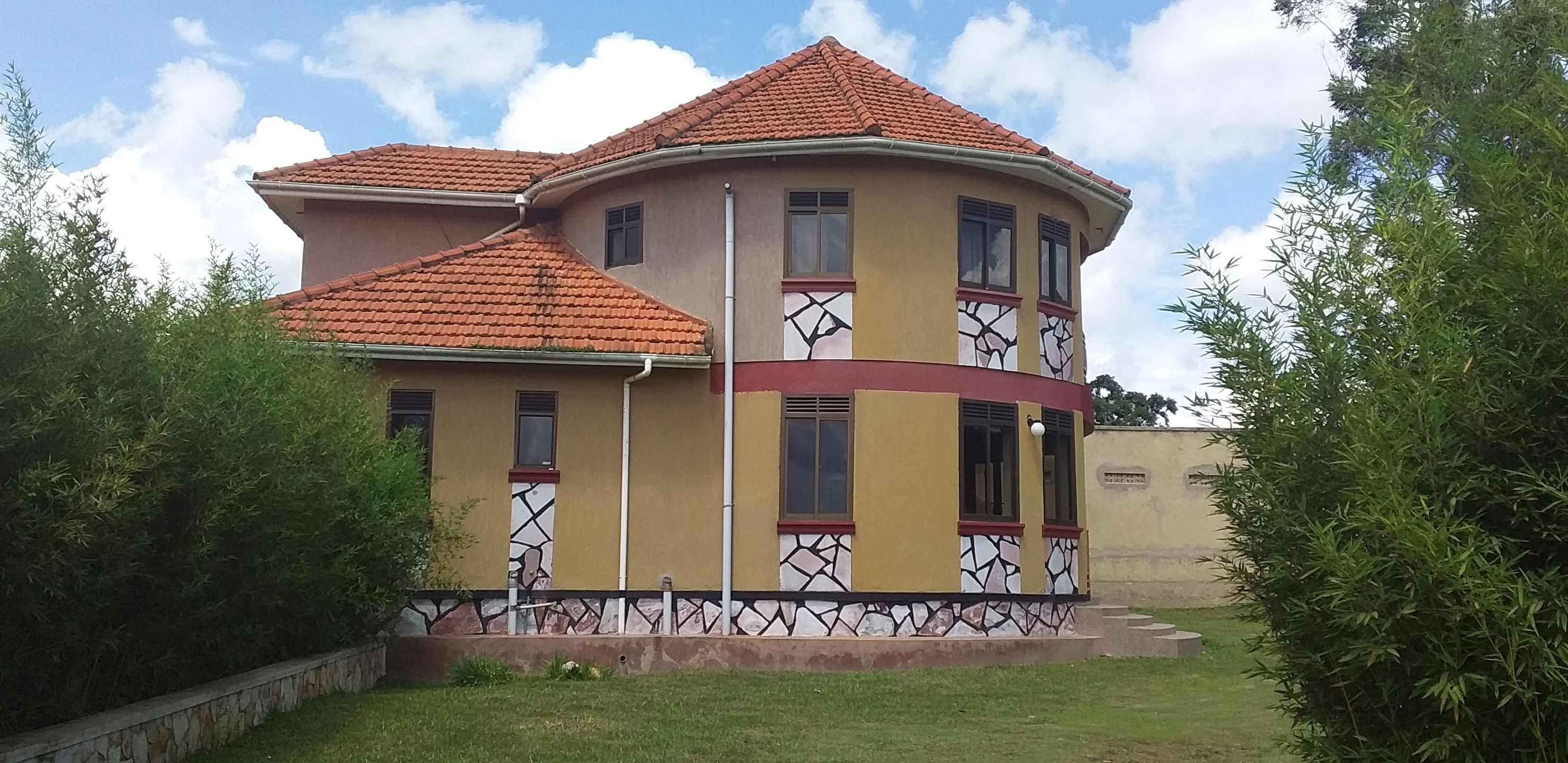 A two-story house with a curved roof, multiple windows, and a stone base.