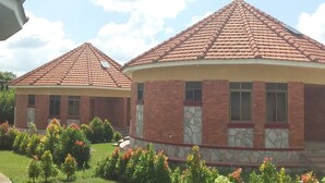 Two buildings with red-tiled roofs and brick exteriors, surrounded by well-maintained gardens. - Mango Cottages & Recreation Center (Kakiri)