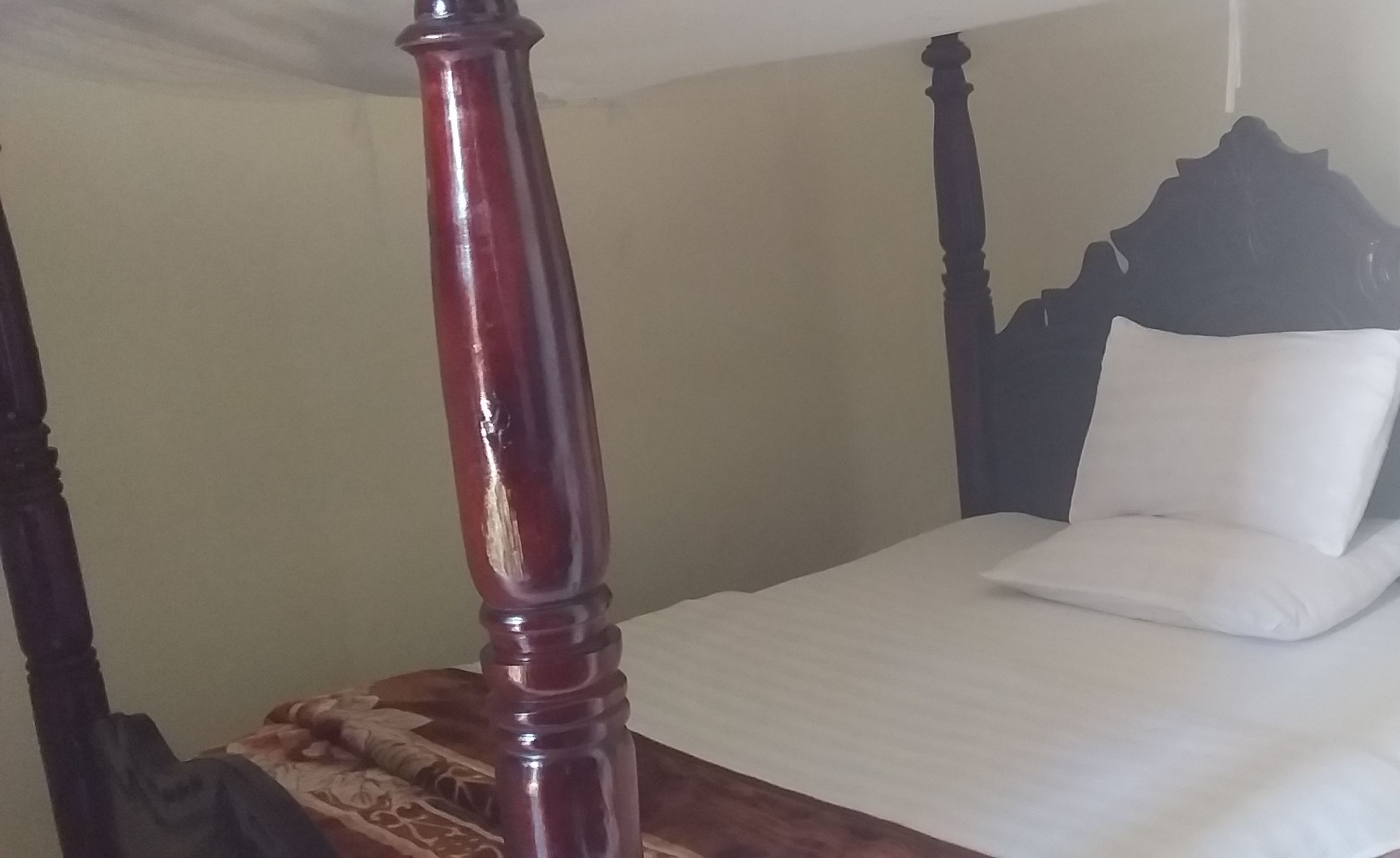 A four-poster bed with a white mattress and a dark headboard.