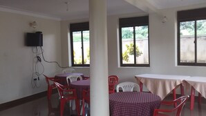 A room with tables and chairs, a television mounted on the wall, and large windows. - Mango Cottages & Recreation Center (Kakiri)