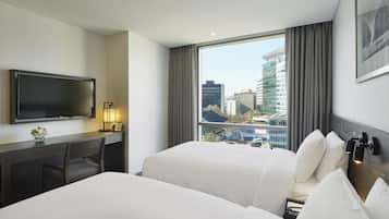 Habitación de hotel con un ventanal grande, un escritorio con televisor de pantalla plana, dos camas y vistas a edificios de la ciudad.