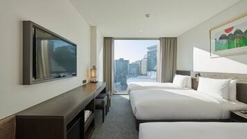 Habitación de hotel con dos camas, televisión, escritorio y un ventanal con vistas a la ciudad.