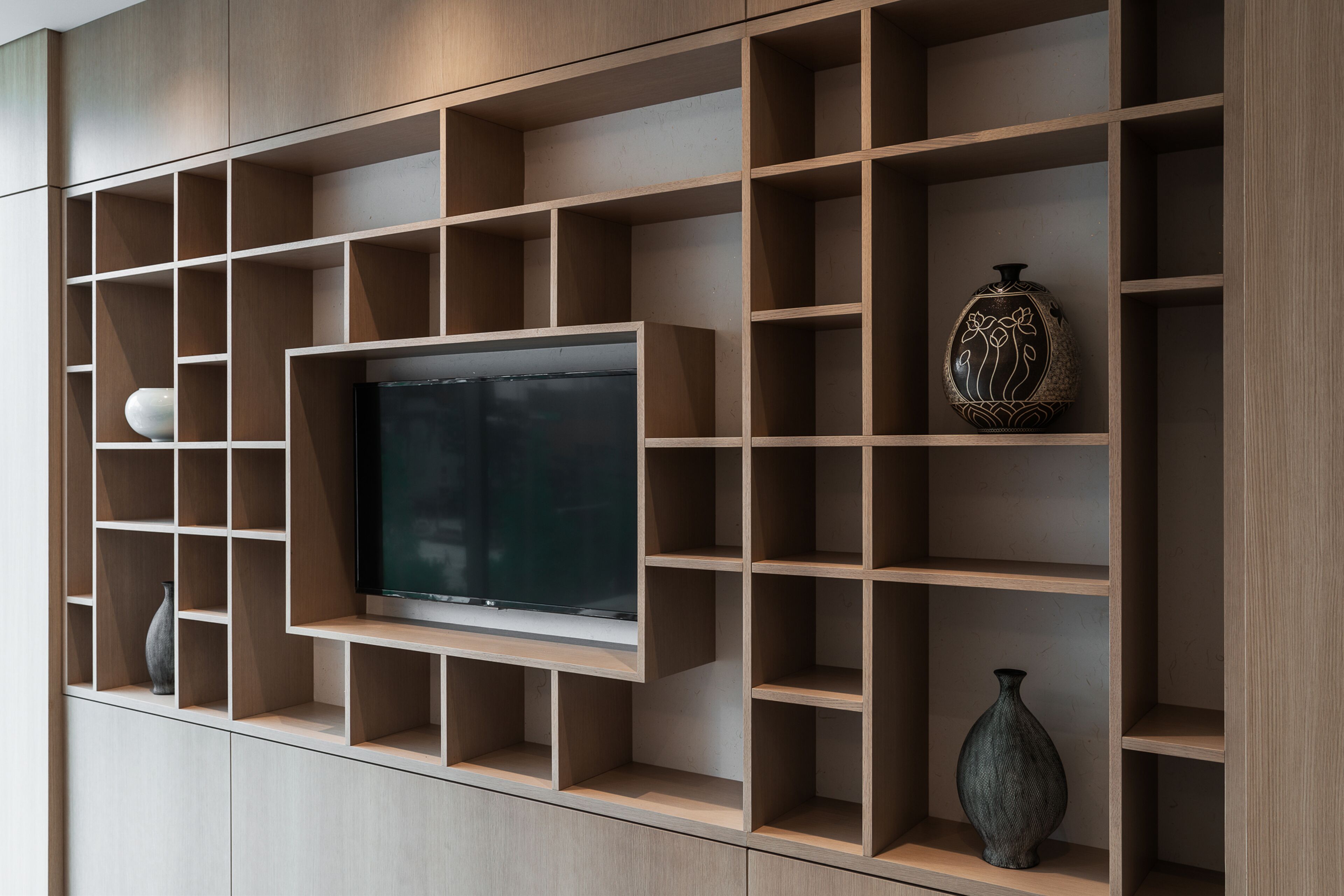 A modern living room with a built-in TV, wooden shelving, and decorative vases.
