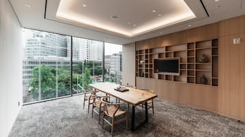 Una sala de conferencias moderna con una gran mesa, sillas, un televisor y vistas a la ciudad a través de amplios ventanales.