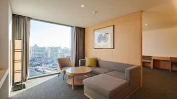 A modern hotel room with a large window, a sofa, a round table, and a city view.