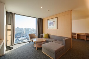 A modern hotel room with a large window, a sofa, a round table, and a city view.