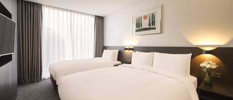 A hotel room with two beds, a large window with curtains, a painting on the wall, and a nightstand with a lamp and flowers.