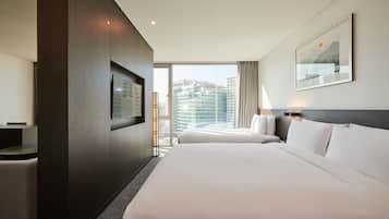 Ein Hotelzimmer mit einem großen Bett, einem Fernseher, einem Schreibtisch und Blick auf die Stadt.