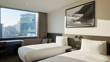 A hotel room with two beds, a desk, and a large window offering a city view.