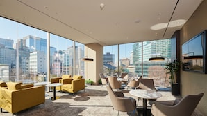 A modern lounge with large windows, yellow sofas, and round tables. - NINE TREE BY PARNAS SEOUL INSADONG (Seoul)