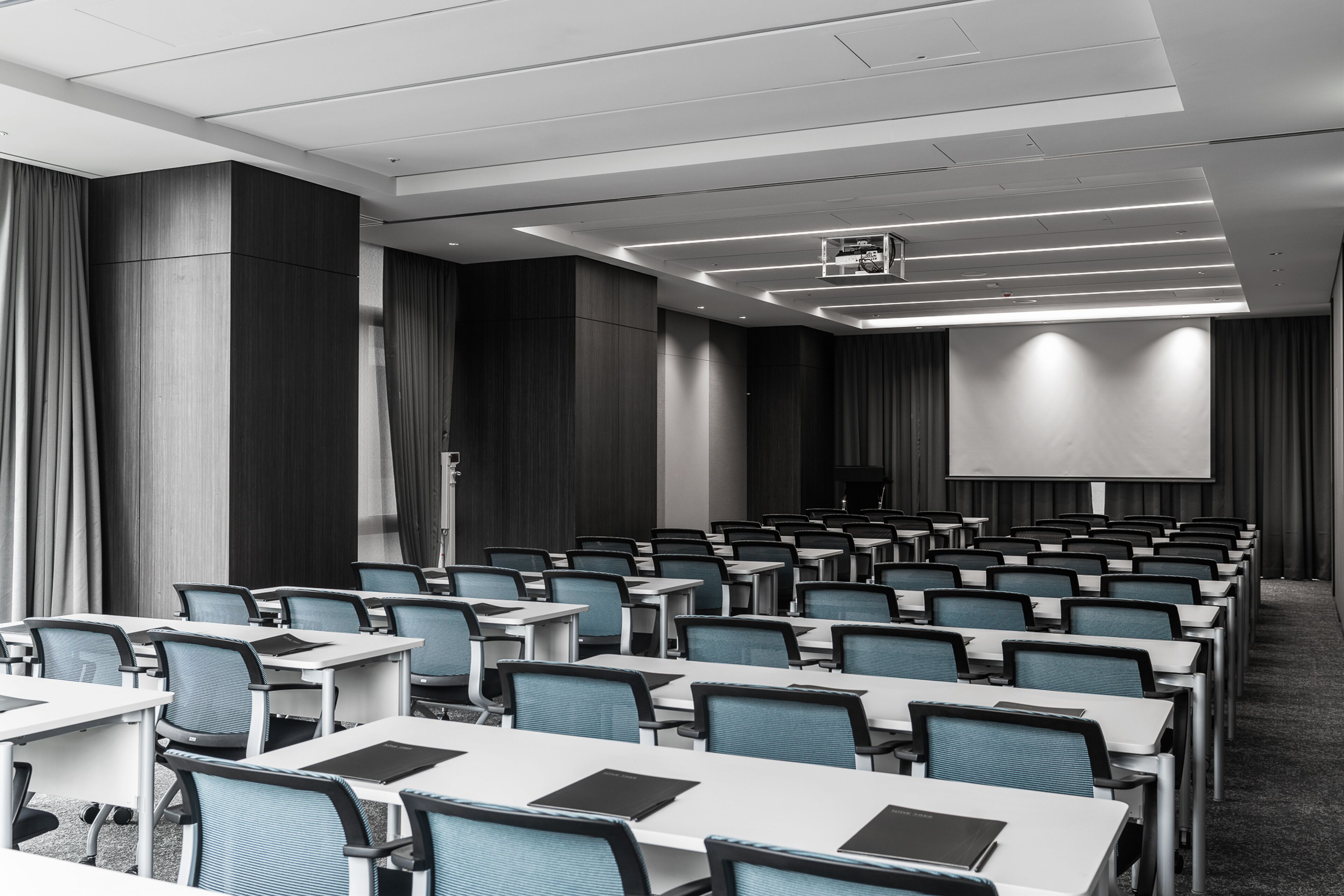 A conference room with rows of tables and chairs, a projector screen, and a large screen at the front.