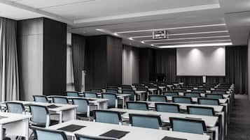A conference room with rows of tables and chairs, a projector screen, and a large screen at the front.