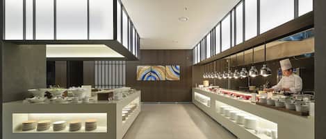 A modern kitchen with a chef preparing food, equipped with stainless steel appliances and a variety of dishes displayed on counters.