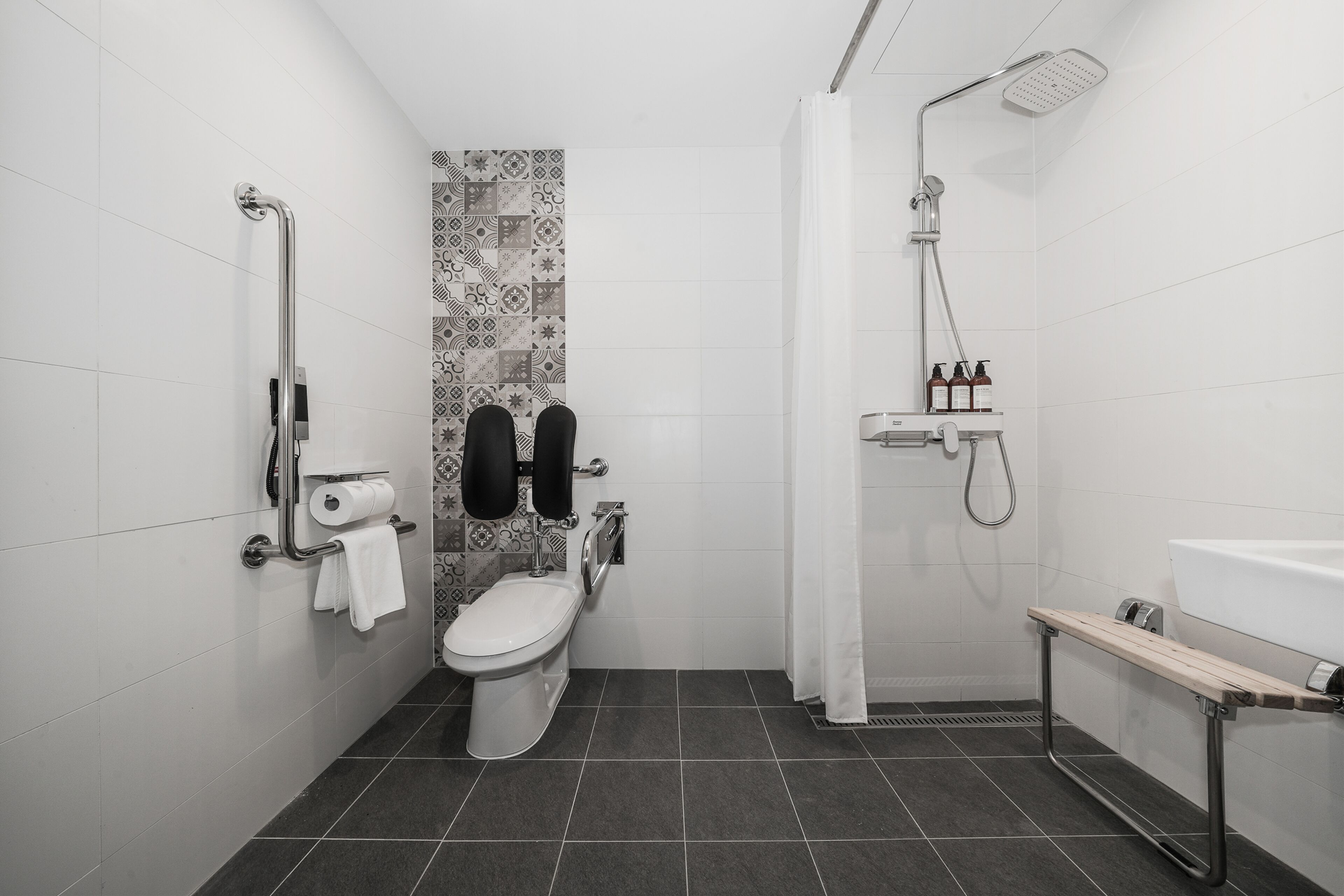 A modern bathroom with a toilet, bidet, shower, and a bench.