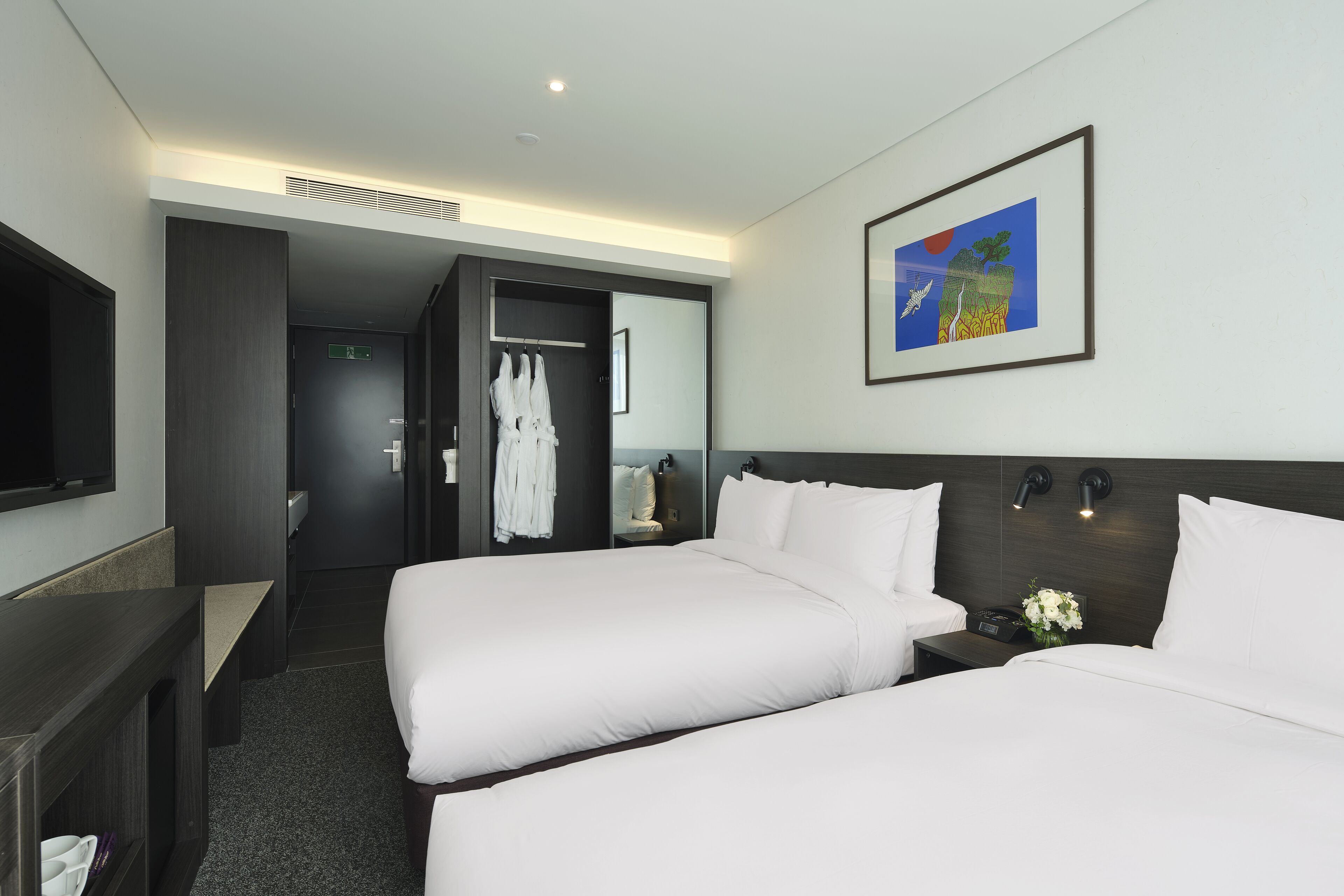 Habitación de hotel con dos camas, televisión, un cuadro y baño con ducha e inodoro.