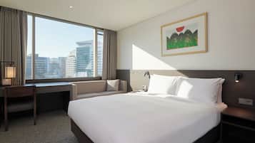 A hotel room with a large bed, a desk, a chair, and a window with a city view.