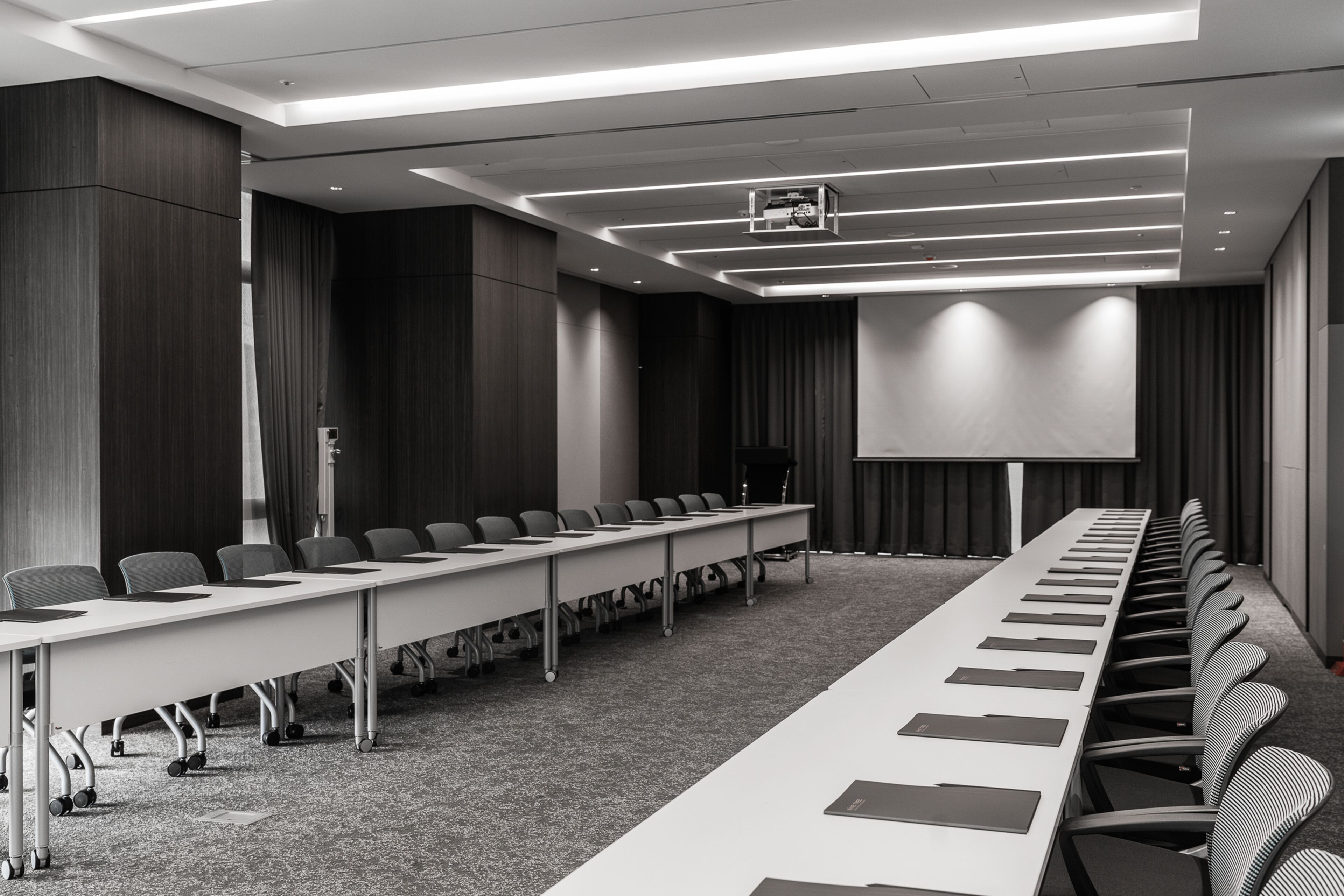 A conference room with a long table, chairs, a projector screen, and a carpeted floor.